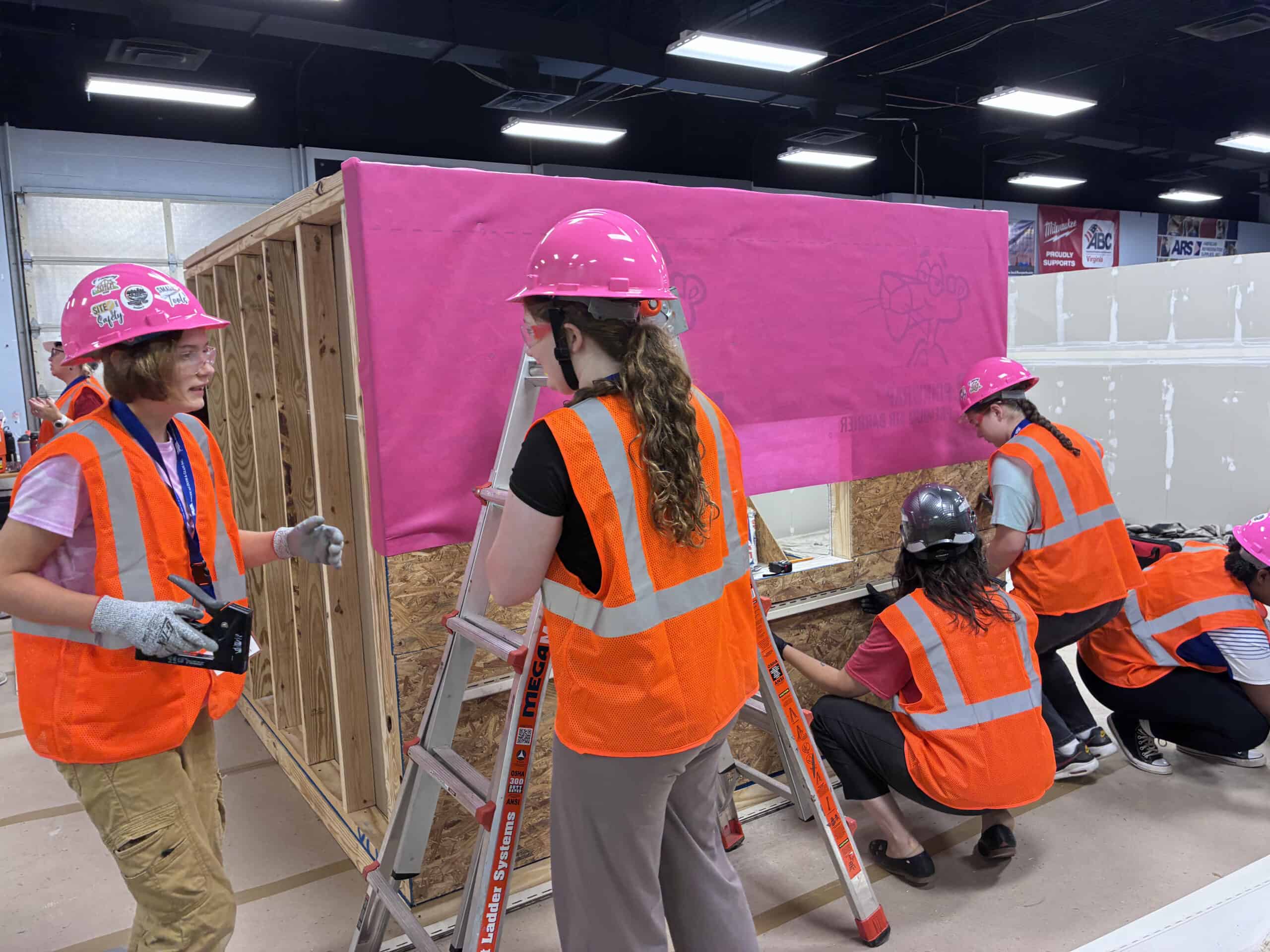 Group of children building a wall with pink insulation at a construction site.