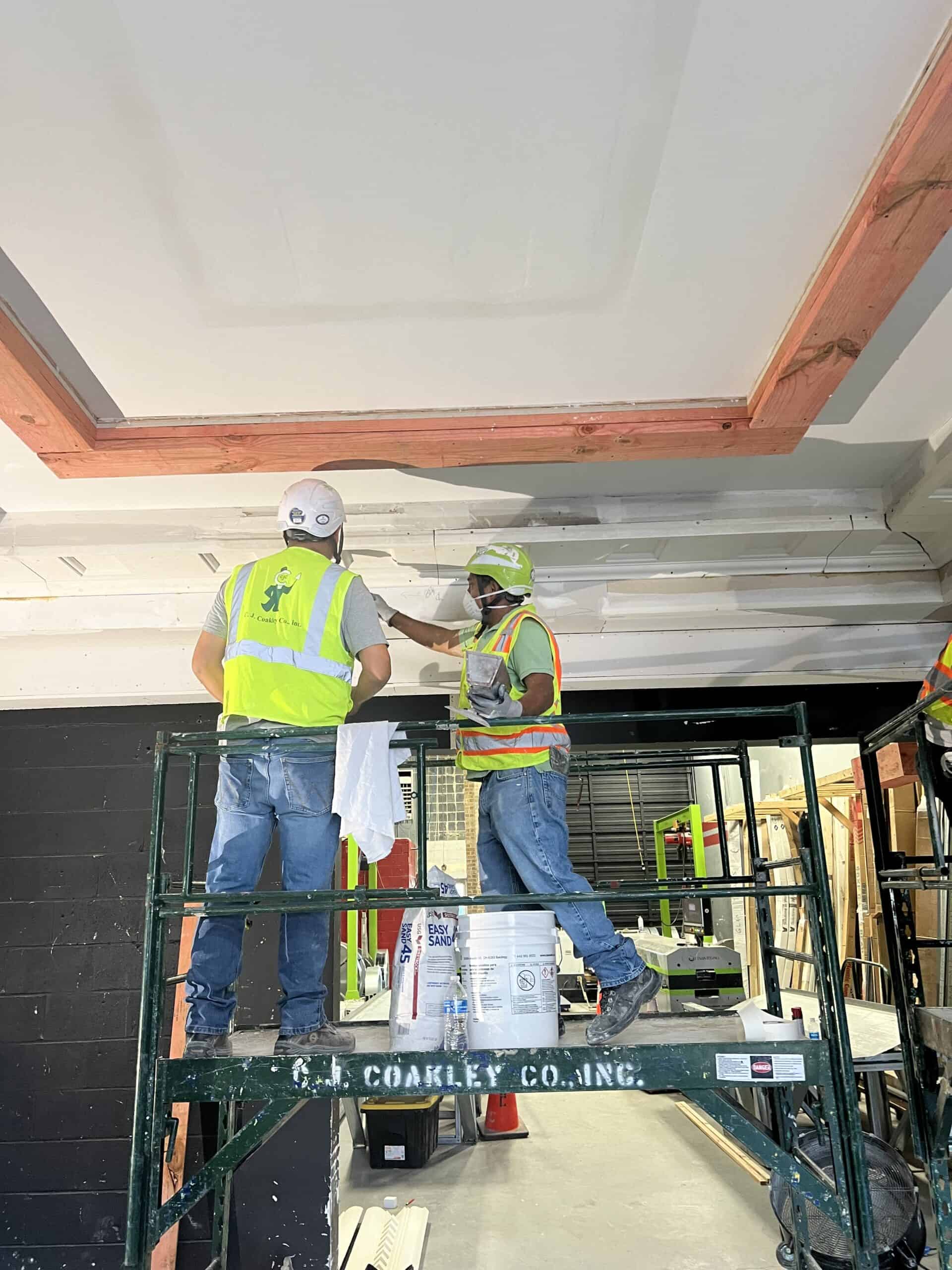 Construction workers installing ceiling panels at NV3C project site.