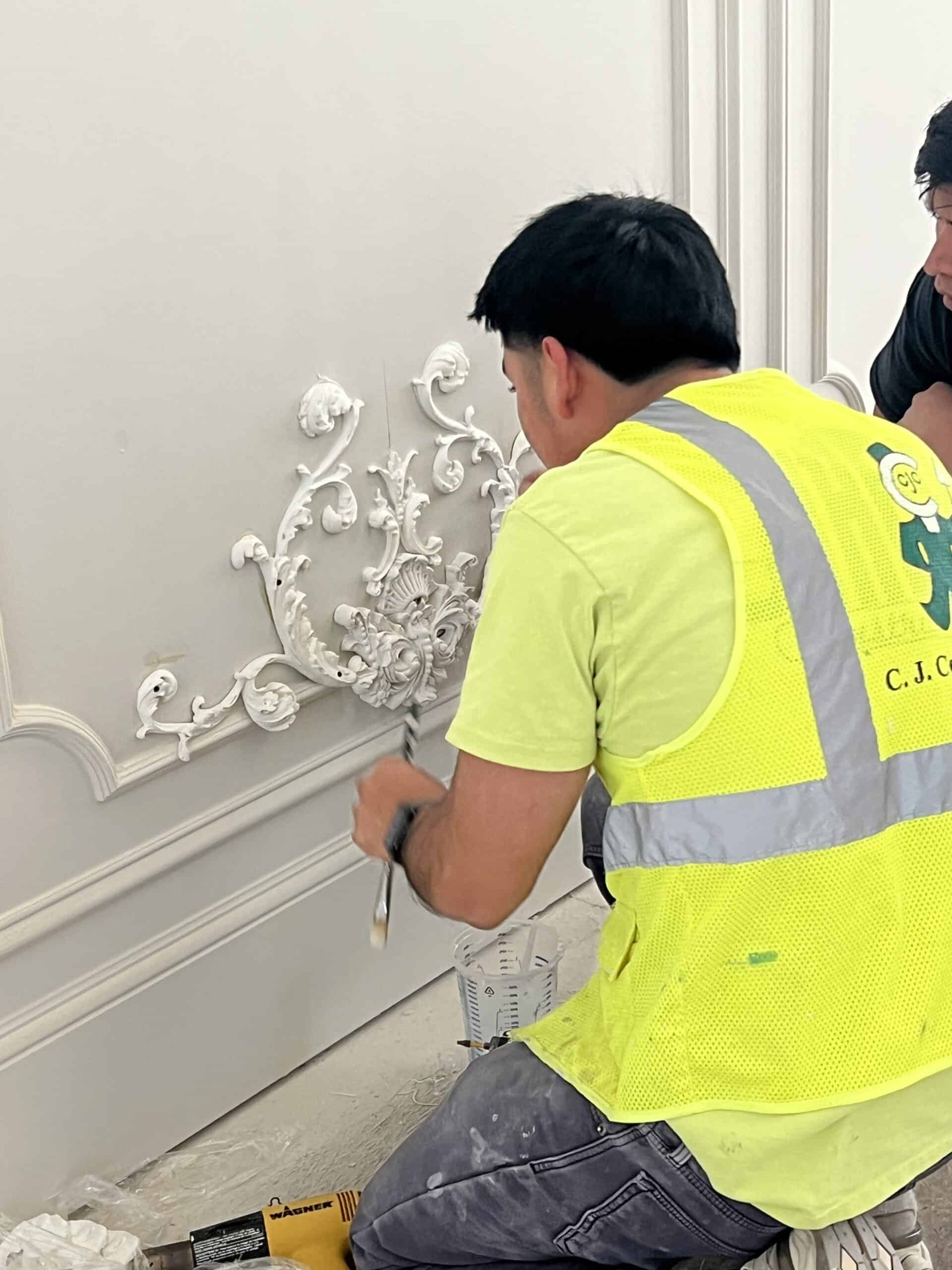 Construction worker installing decorative wall molding in interior space.