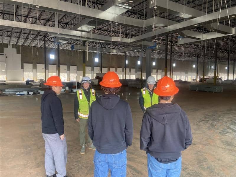 Construction workers in safety gear inspecting a large industrial building.
