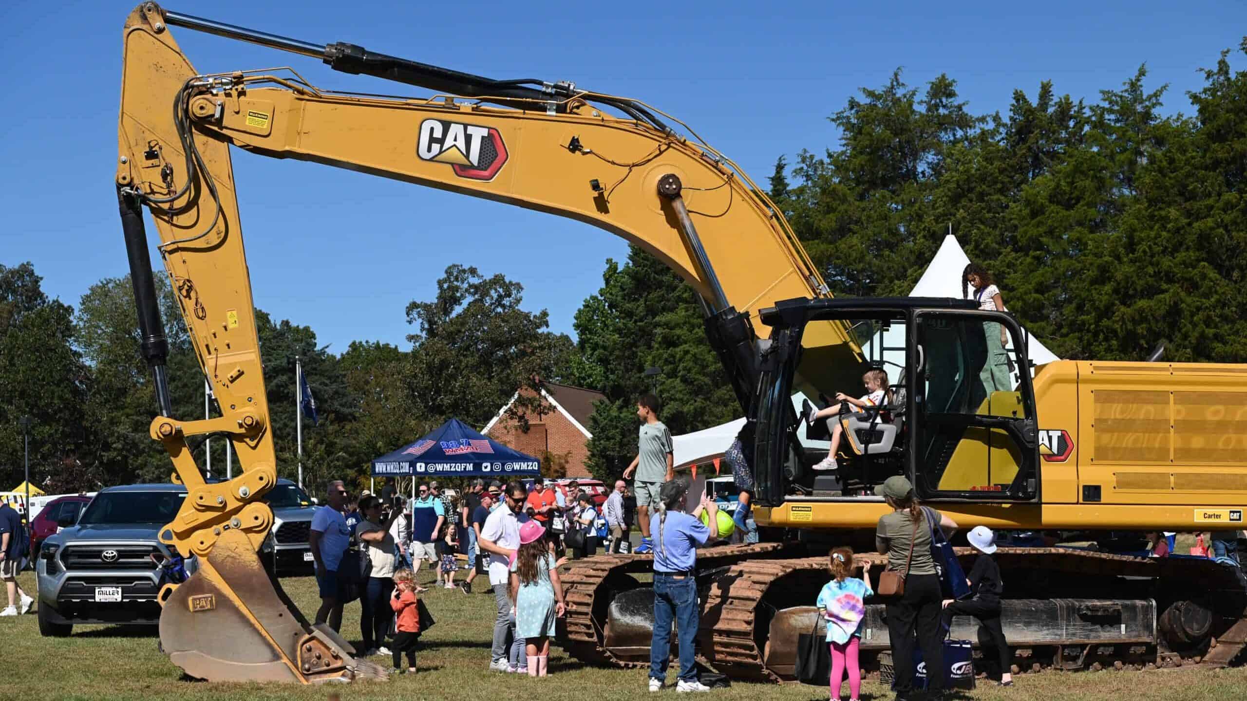Large yellow CAT excavator at outdoor event with people and tents.
