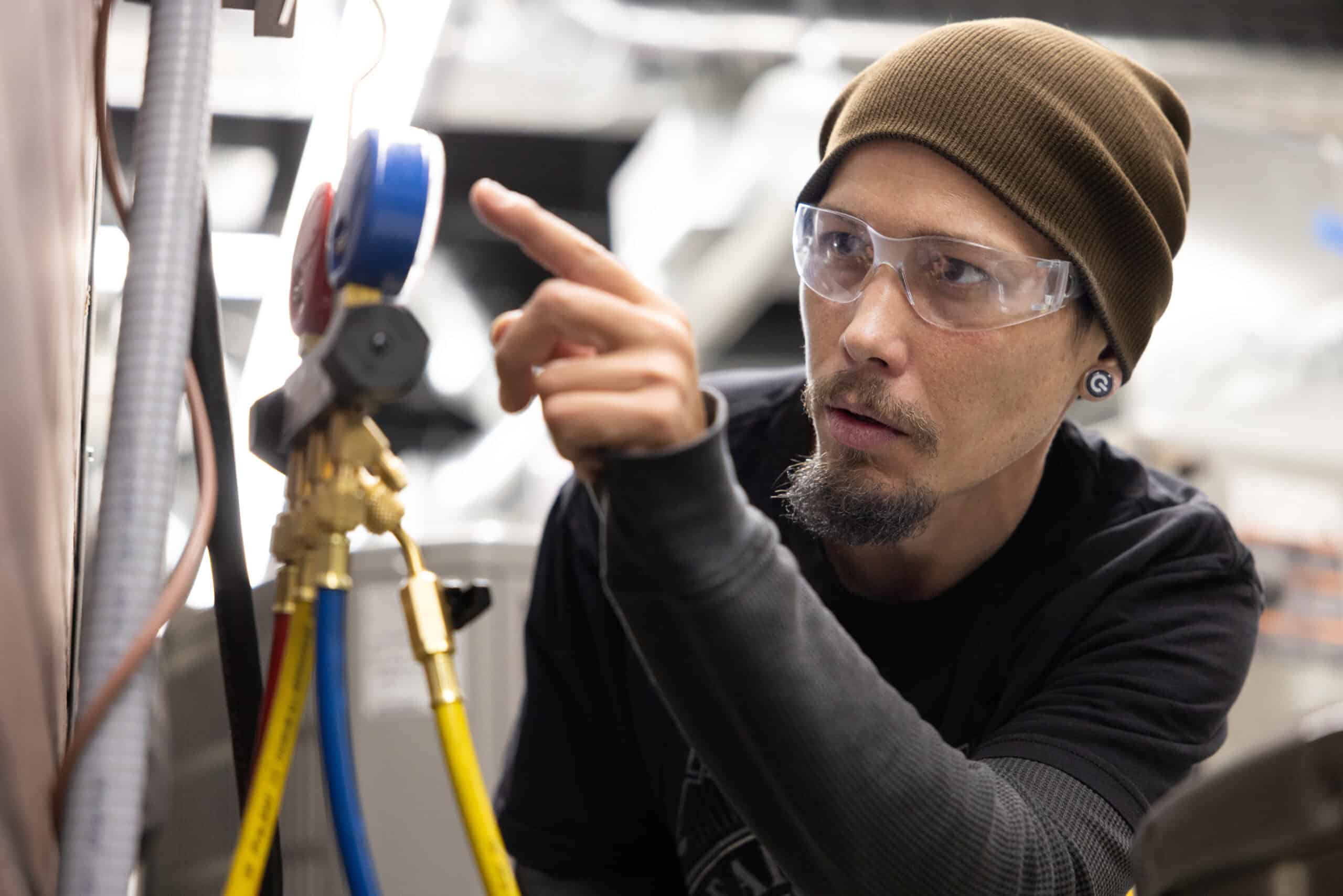 Technician inspecting industrial equipment with gauges and hoses in a factory setting.