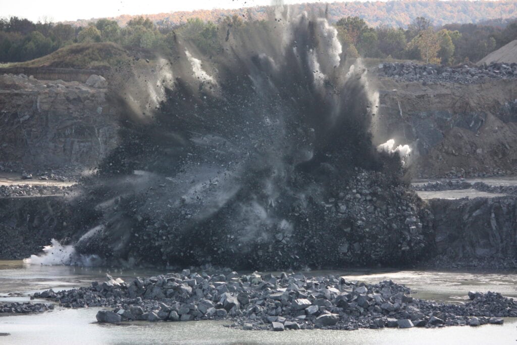 Explosion in a quarry with water and rocks flying in the air.